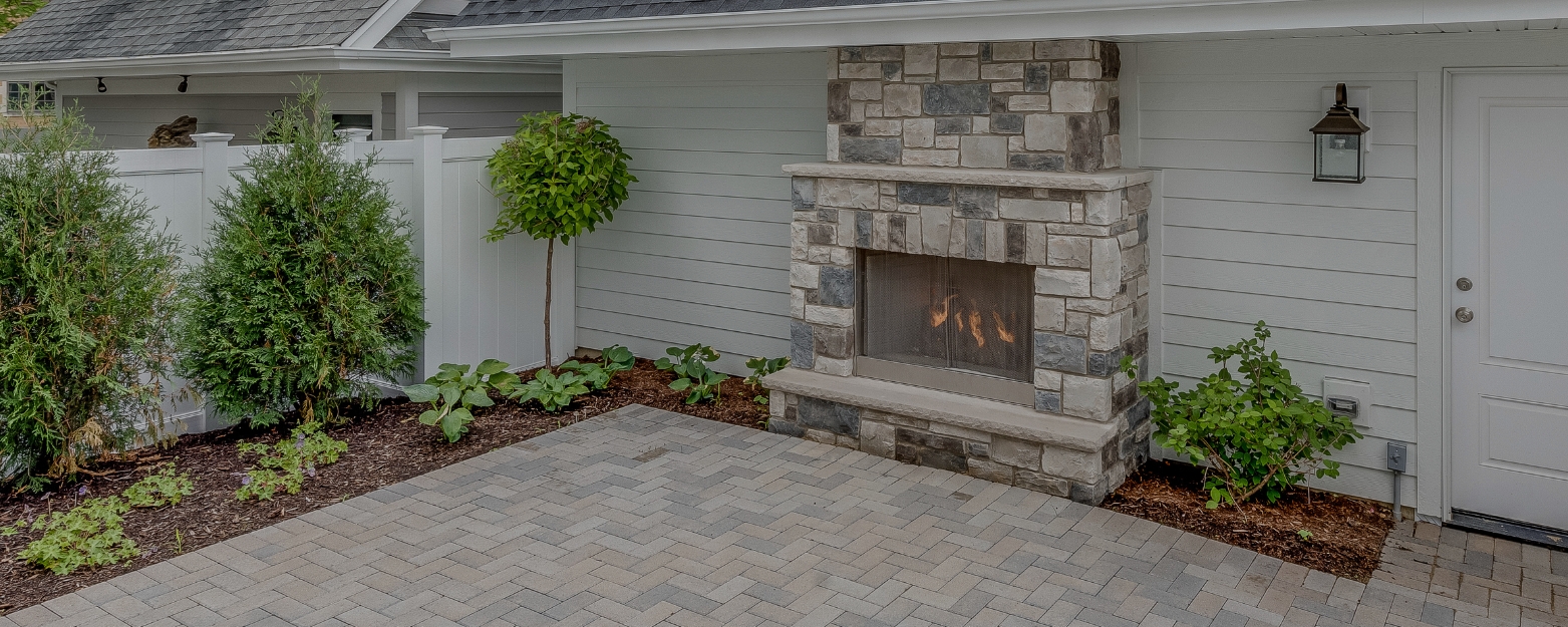 Outdoor stone fireplace with custom masonry and a herringbone paver patio in a beautifully landscaped backyard in Redmond, WA.